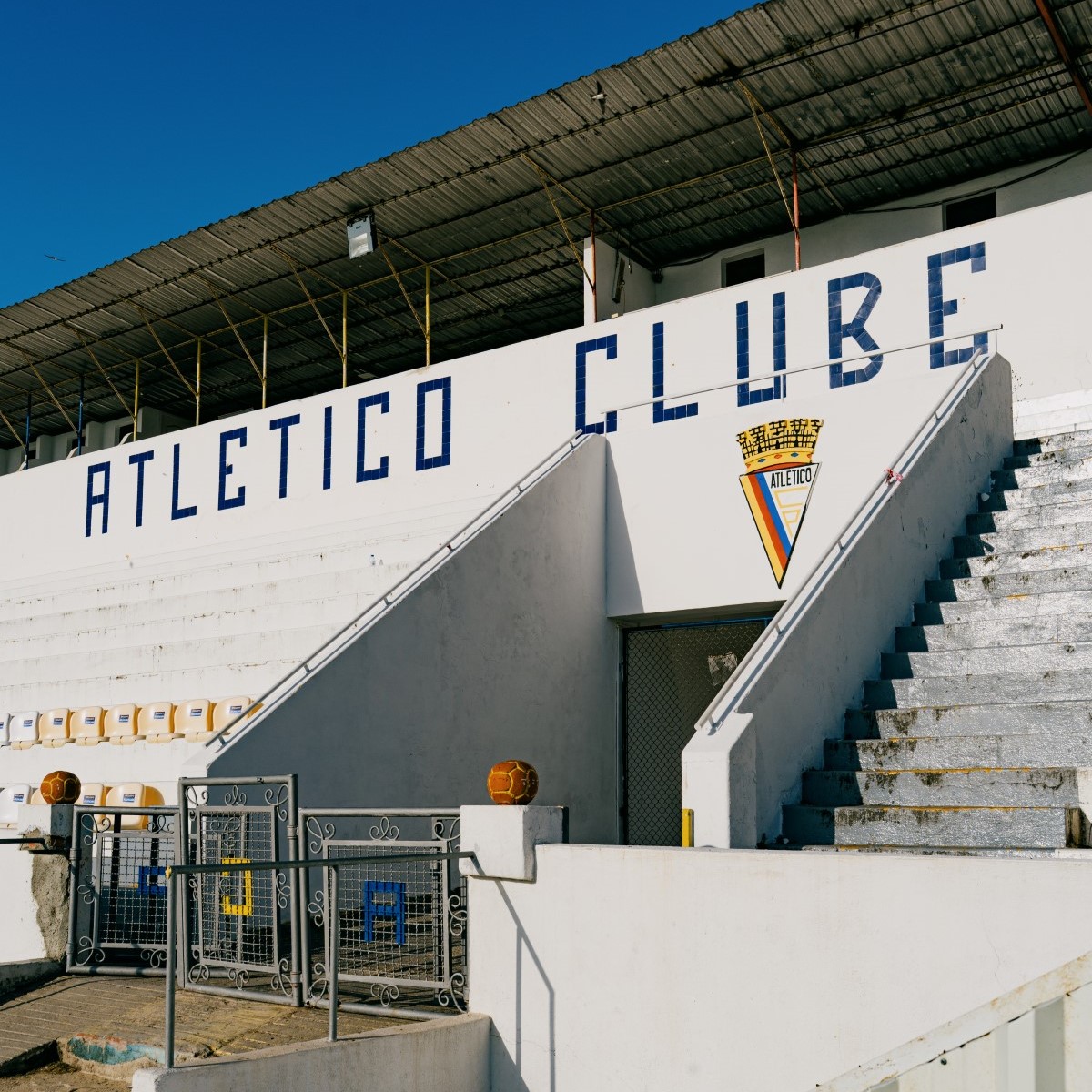 Túnel central de acesso ao relvado e bancada principal do Estádio da Tapadinha, com o emblema e o nome do Atlético Clube de Portugal visíveis na fachada.