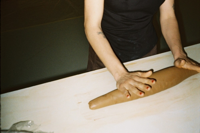 Detailed view of hands shaping a piece of clay on a workbench.