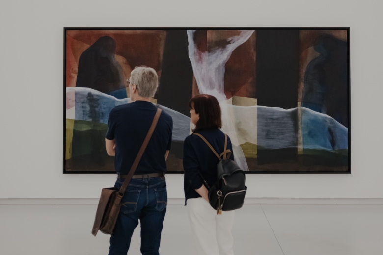 Dois visitantes observam uma pintura monumental de Pedro Cabrita Reis, composta por formas abstratas e áreas de cor sobrepostas em tons profundos de azul, preto, branco e castanho, exposta no MAAT Gallery.