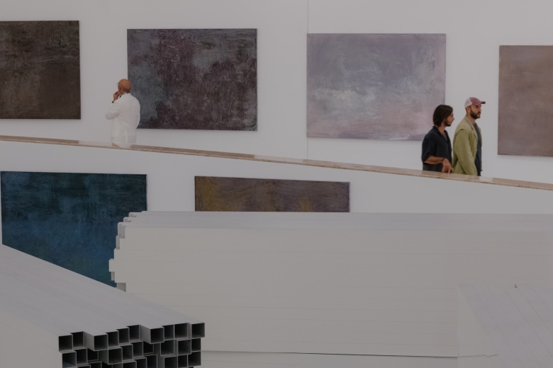Vista da rampa da Galeria Oval do MAAT com pinturas abstratas de grande formato de Pedro Cabrita Reis; duas pessoas percorrem o espaço enquanto outra observa atentamente uma das obras.
